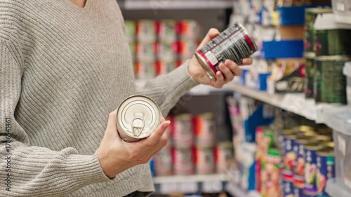 A woman choosing canned dog or cat food at a pet store, reading the label. Customer compares wet dog or cat food in the aisle with various canned goods on the shelves. Concept of responsible pet owner