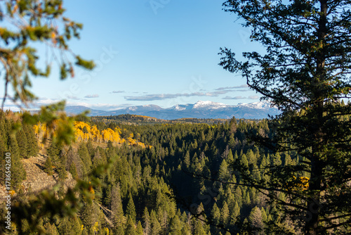 Autumn colors spread across a forested valley with snowcapped mountains rising in the distance.
