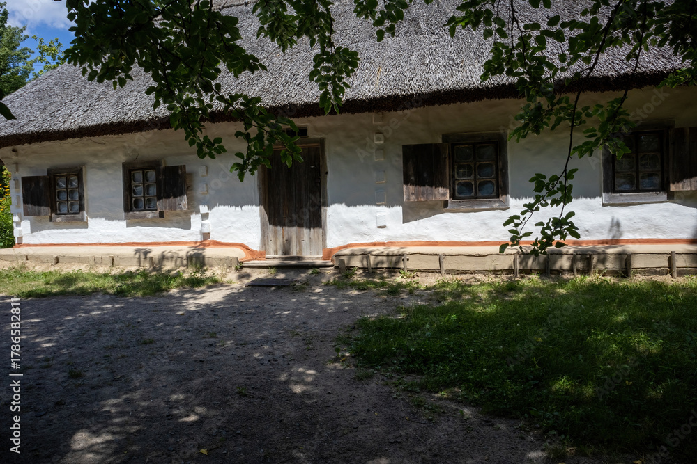 Fototapeta premium Traditional rural house with white walls and thatched roof in summer