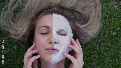 Close-up of a young woman lying on her back with a cosmetic face mask, gently massaging her skin. Perfect for skincare, beauty, wellness, and spa-related video projects.
