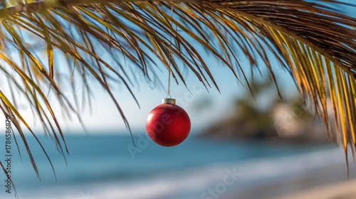 Fototapeta Naklejka Na Ścianę i Meble -  Single red Christmas ornament hanging from palm tree branch. Tropical beach panorama background