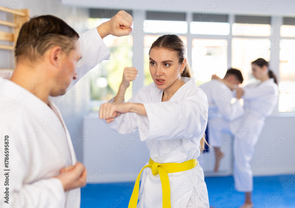 Obraz premium Adult man and young woman karatekas train karate in group in studio..