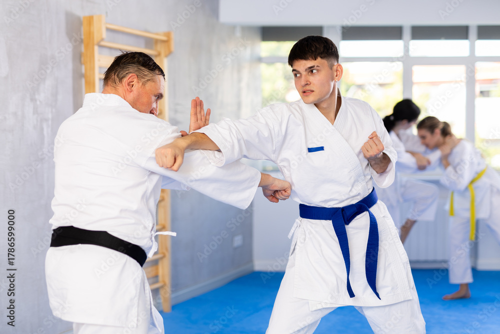 Fototapeta premium Active young male attendee of karate classes fighting with middle-aged man during workout session