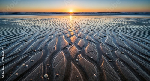 Fototapeta Naklejka Na Ścianę i Meble -  Golden sunlight reflecting on the wet sand at low tide during sunset