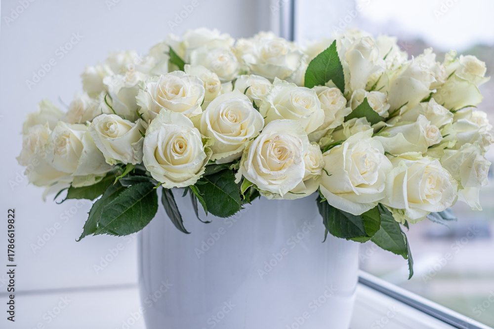 Obraz premium White roses arranged beautifully in a modern vase, creating an elegant floral decoration for celebrations, anniversaries, and special occasions with a soft background ambiance