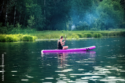 A woman sup surfing paddling on a boat on a river on sunny day.