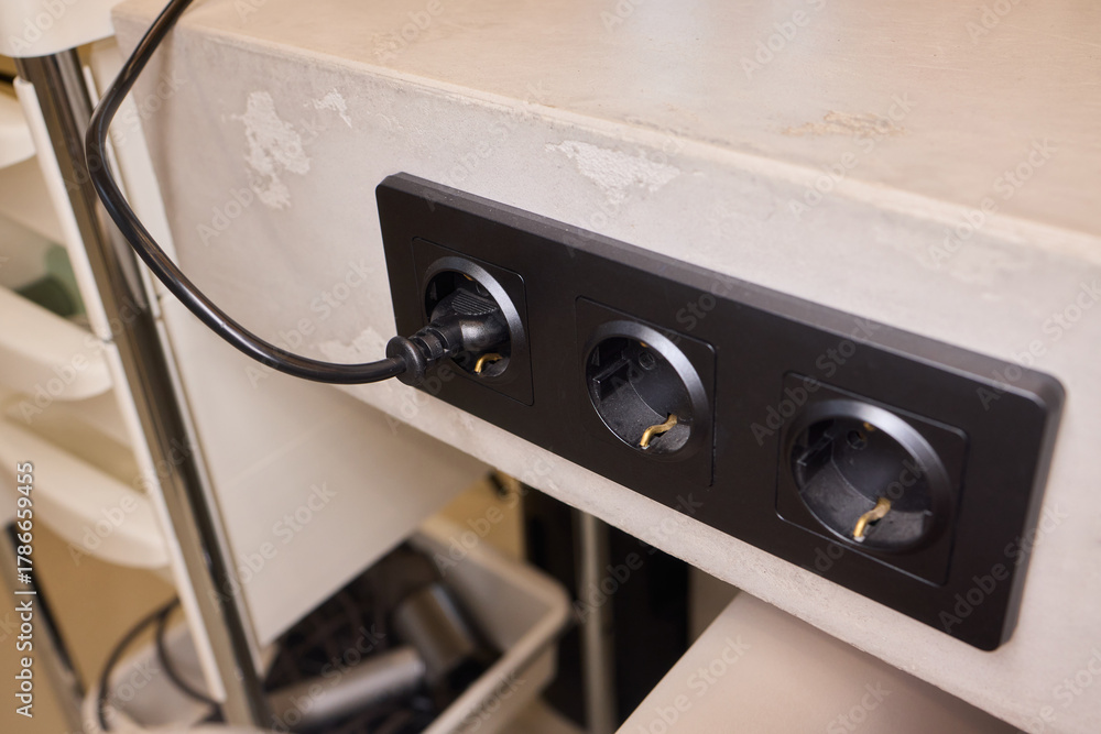 Fototapeta premium Power hub setup, Closeup of mounted power strip with multiple connections and cables, IT technician arranging cords and connecting devices on cluttered tech workstation