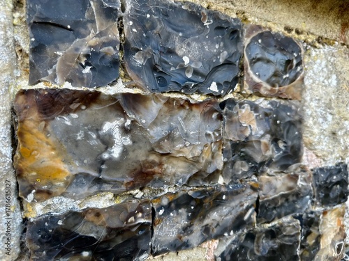 Close view of knapped flint blocks set in limestone, forming the medieval chequerboard masonry of Saint-Martin Church in Saint-Valery-sur-Somme, Picardy, with glossy textures and weathered patina
