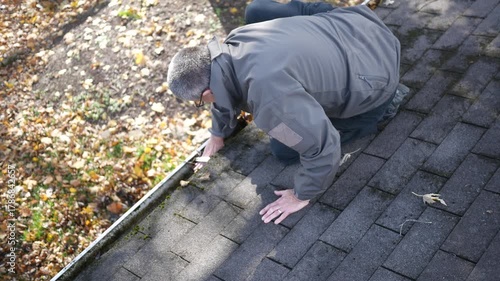 Older Man Cleans Gutters on Roof of House.
