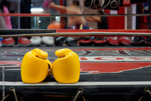 Bright Yellow Boxing Gloves Resting on a Ring Apron. Closeup of vibrant yellow boxing or Muay Thai gloves placed on the edge of boxing ring with blurred action of preparation and martial arts training