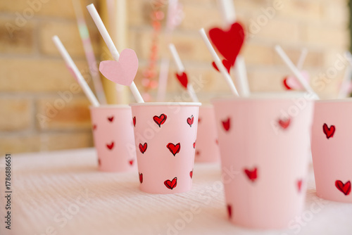 Set of paper cups with small red heart designs and straws.