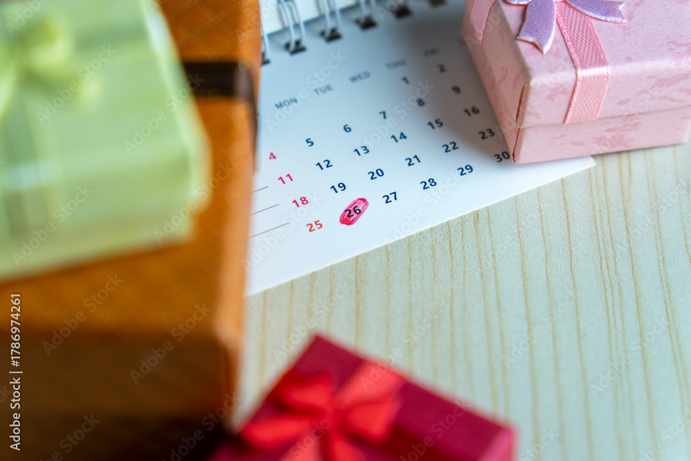 Obraz premium Close-up of a calendar with the 26th date circled in red surrounded by colorful gift boxes. Boxing Day celebration and post-holiday sales concept.