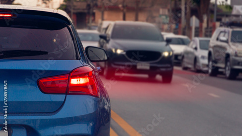 Luxury of blue car on the road with speed light red color from brake. Other car driving passthrough from opposite lens. and many cars parking side of asphalt road.