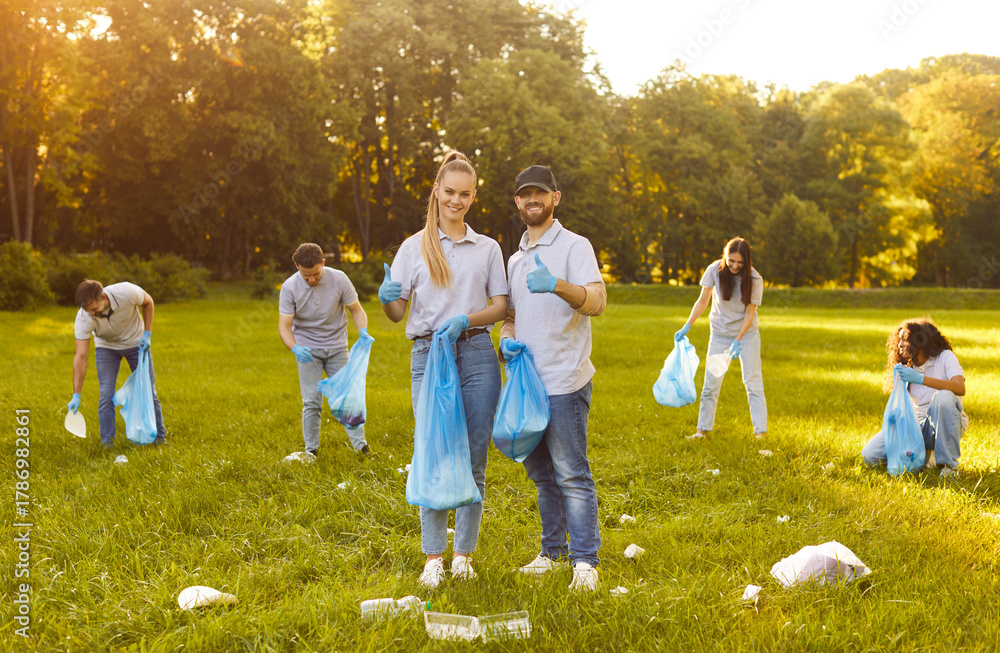 Fototapeta premium Happy volunteer group, friends working happily in sunny green park, diverse team smiling, holding bags and wearing gloves, feeling accomplished volunteering and cleaning environment, thumbs up showing