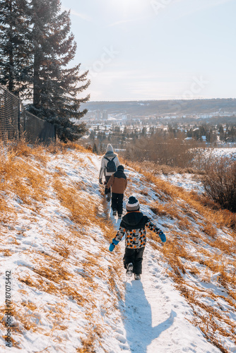 Woman and children walking on a snowy footpath in a park on a sunny winter day