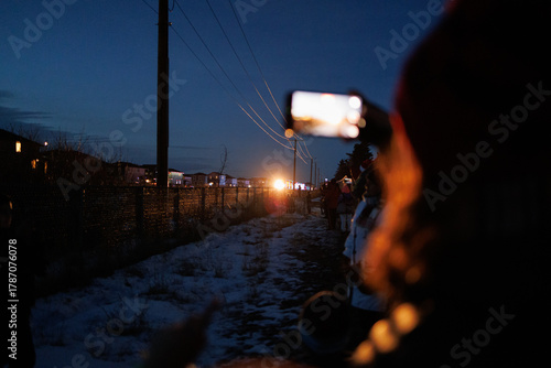 Woman taking pictures on her smartphone of a coming holiday train in the distance at night