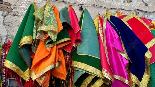 Konstfotografi A vibrant assortment of traditional ethnic textiles, likely Indian or Middle Eastern garments such as lehenga cholis, dupattas, or religious deity clothing, hangs on display