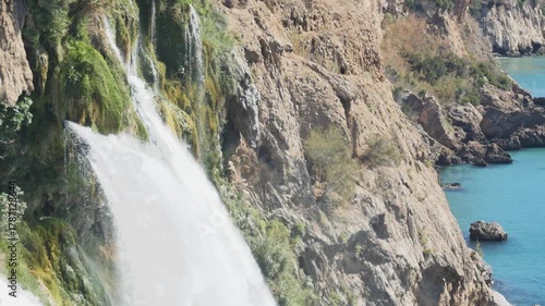 A detailed view of the Lower Düden Falls, showcasing the geological layers and the vibrant green moss and vegetation clinging to the towering brown cliffs.