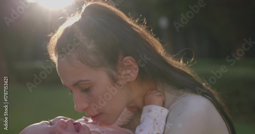 Mother girls infant daughter a big kiss on the cheek at park during sunset - close up