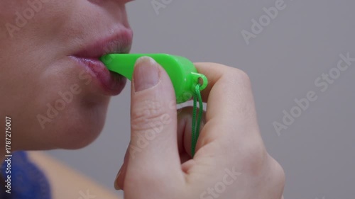 A green plastic whistle is held and blown into. The person is performing a long, drawn-out whistle.