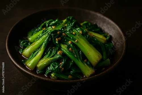 Stir-Fried Baby Bok Choy with Garlic and Sesame Seeds in Dark Ceramic Bowl – Asian Vegan Cuisine on Dark Background, Healthy Food Photograph