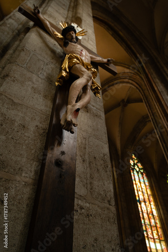 Kutná Hora, Czech Republic – August 8, 2025: Dramatic perspective of Jesus Christ sculpture on the cross with ornate gold leaf details and stained glass windows, Saint Barbara’s Cathedral, Kutná Hora