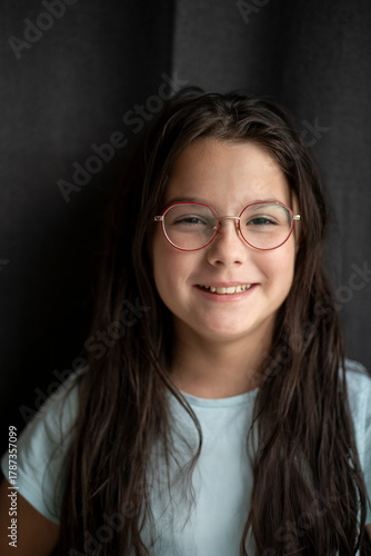 Smiling girl with long hair and glasses showing her teeth against a dark fabric background, soft light, copy space. Concept of dental health, confidence