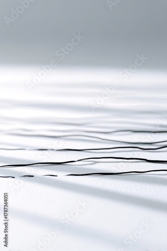 Thin, wavy black lines are arranged horizontally on a textured white surface, creating an abstract, minimalist composition with soft, diagonal shadows.