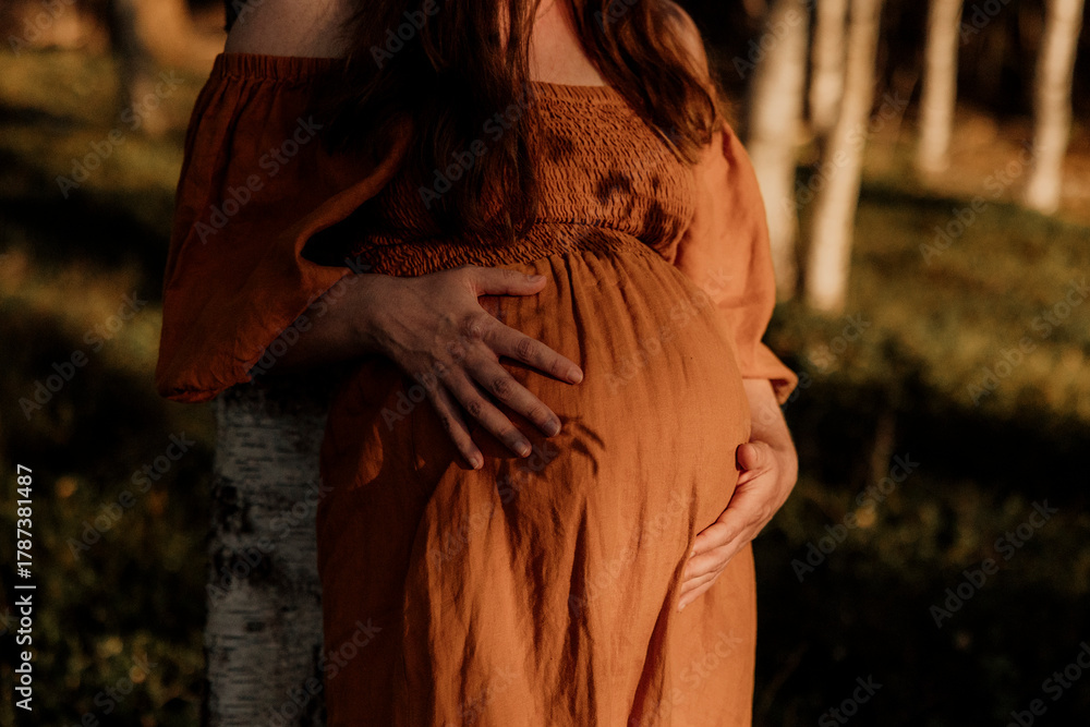 Naklejka premium Pregnant woman in orange dress holding belly outdoors