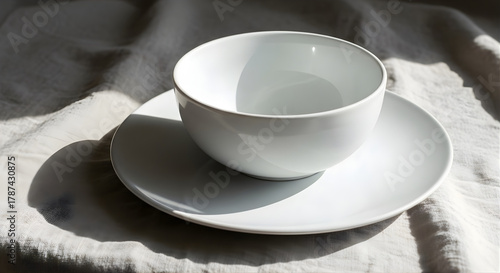 White ceramic bowl and plate on soft linen fabric under natural light