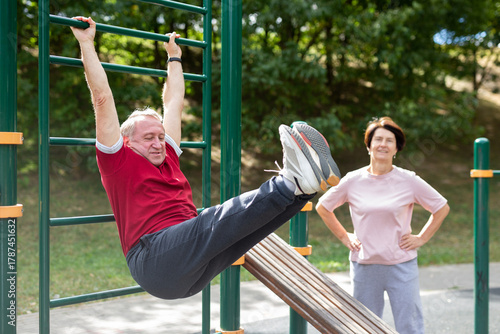 Aged man and woman doing exercises on sports bars in open-air sports area