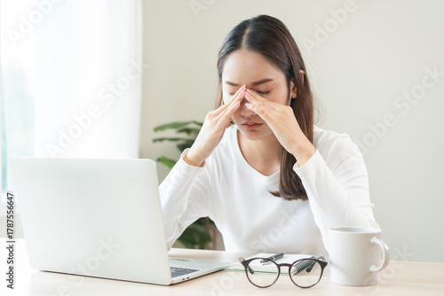 Fotografia Eye problem concept, fatigue asian young woman tired eyes, irritated rubbing nose, relief vision pain after work on laptop computer, eye strain, take out glasses on table, suffer migraine, bad blurry