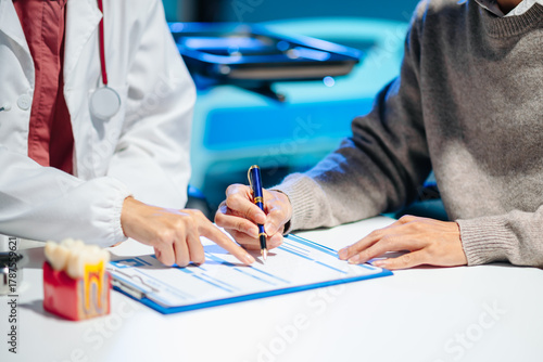 Asian female dentist explains dental model and treatment form to patient during consultation