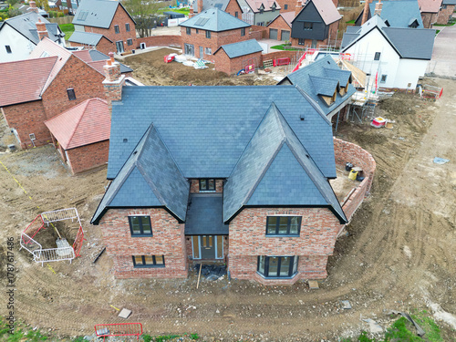 Newly completed large detached family home seen near other private and affordable homes in a British housing development site. Seen with other near completed family homes.