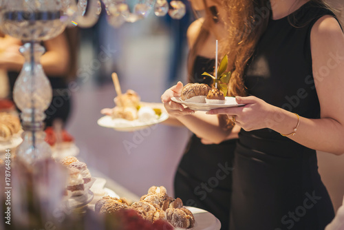 Elegant women enjoying a dessert display at a luxurious event in a well-lit venue during the evening