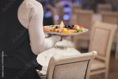 Waiter carries a seafood platter with fresh shrimp, lemon slices, olives, and herbs in an elegant restaurant setting during dinner time
