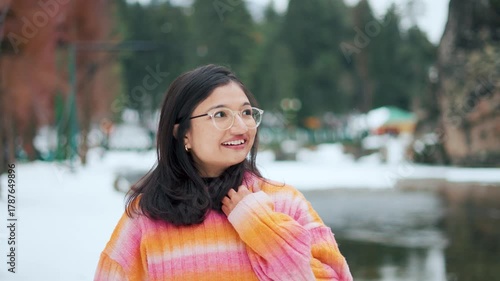 4K Portrait of teenager Indian girl wearing colorful sweater enjoying winter holidays at Betab Valley, Kashmir, India. Winter holidays. Tourist at snow covered mountain valley with river beside. 