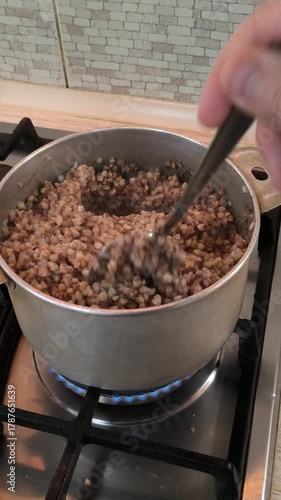 Buckwheat in a saucepan. A person is cooking porridge on the stove. Home cooking. Buckwheat porridge.