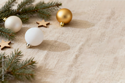 Cozy Christmas baubles, fir branches, and wooden stars on natural beige linen background. Minimalist holiday flat lay with copy space. winter season greetings.