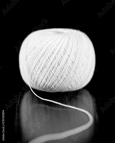 A skein of white thread lies on a dark wooden table. Selective focus. Close-up.