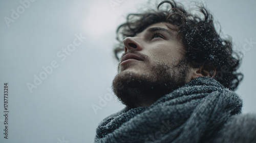 Young man with snowflakes on face gazes upwards with hope and determination in winter