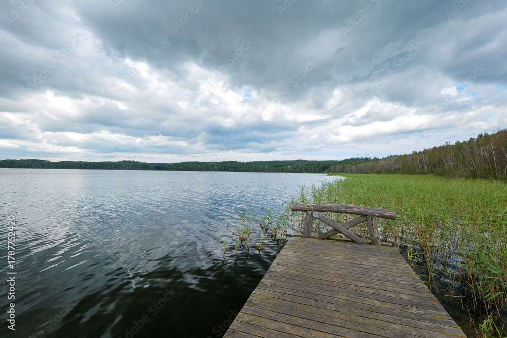Naklejka premium A beautiful lake nestled amidst a forest. A wooden jetty is in the foreground. Lake Choczewo, Pomeranian Voivodeship, Choczewo, Poland. Kashubia region.