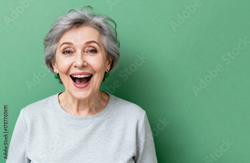 Portrait of a happy elderly woman with gray hair, smiling broadly on a green background