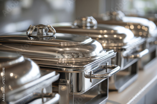 A row of shiny stainless steel buffet chafing dishes with lids neatly lined up on a banquet table for catering or event service setup