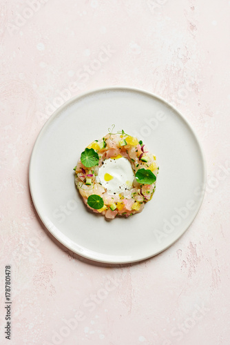 Overhead shot of snapper crudo (raw fish) with coconut, finger lime, cucumber, yuzu, yellow chilli oil and nasturtium leaves, on a pink surface with copy space