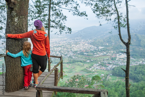 Mother wit kids relaxing on wooden platform high in the pine forest near Batu, East Java. Surrounded by trees and overlooking a scenic valley, this serene viewpoint is perfect for family travel hikes.
