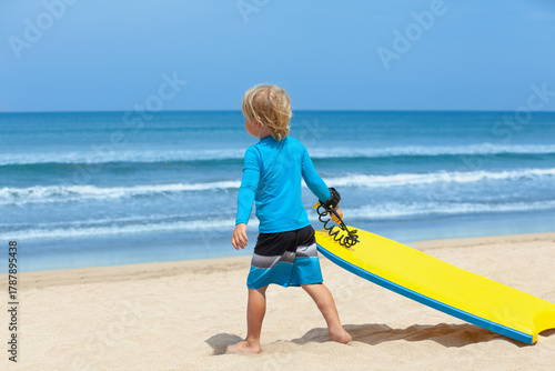 Portrait of little surfer boy with bodyboard have fun on beach, walk by white sand beach. Summer adventures, active families, parents and kids lifestyle, sports activities on school holiday with kids