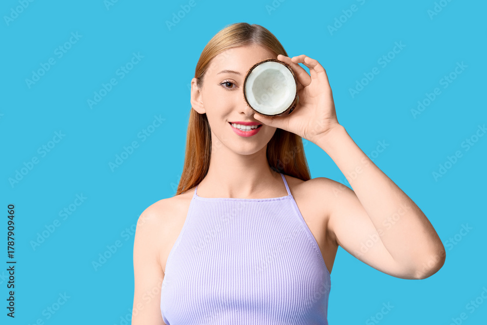 Obraz premium Beautiful young happy woman in stylish summer outfit with half of coconut on blue background