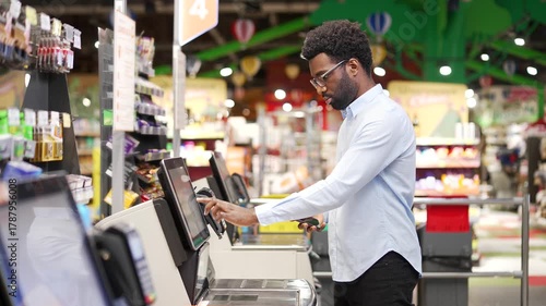 African american male shopper using a self-service cashier checkout in supermarket. Customer scanning produce items using at grocery store cash register. Man uses a terminal to pay for products online