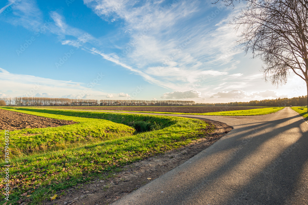 Obraz premium Backlit photograph of an agricultural landscape with ploughed fields, country roads and a ditch.